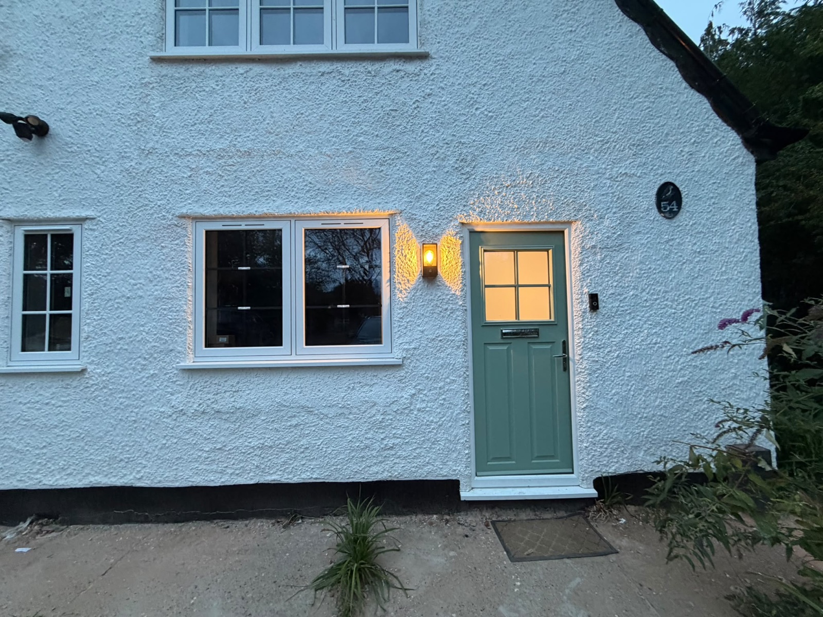House entrance at dusk with wall lights and lit windows