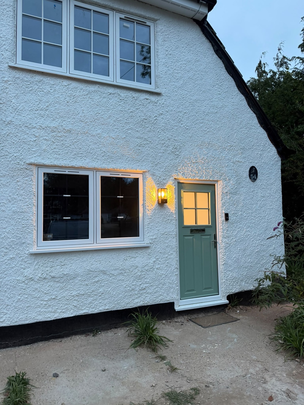 Cottage entrance at dusk with a wall light and lit windows
